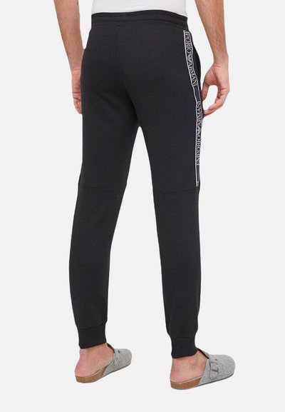 Pantalons de jogging noirs ajustés, avec un marquage latéral blanc et un tissu doux et texturé. Taille élastique et chevilles resserrées.