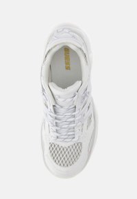 Baskets de sport blanches en mesh et cuir, bout arrondi, semelle épaisse blanche et fermeture lacée. Logo "GUESS" visible en or.