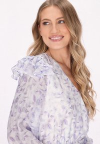 Blomstret omslagskjole i let, gennemsigtigt stof med bølgede lavendelsleeves og en blød farvepalette af lilla og hvid.