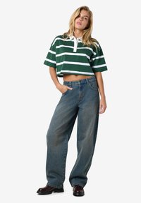 Grønn og hvit stripete kort polo-skjorte med to-knapps placket, kombinert med løstsittende falmede blå jeans og mørke støvler.