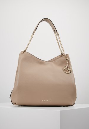 Sac à main en cuir beige avec bandoulière en chaîne dorée et breloque logo Michael Kors, placé sur un socle blanc sur fond uni.