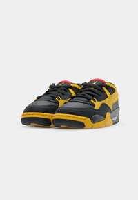 Svarte og gule sneakers med teksturert overdel, med polstret tunge, svarte snøringer og røde detaljer. Lufteputesystem i sålen.