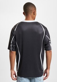 Juoda trumpa rankovė džersio marškiniai su baltais šonų srityje ir apykakle. Pagaminti iš sklandžios medžiagos, pasižymi laisvu siluetu ir apykakle.