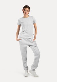 Camiseta de algodón gris con cuello redondo y mangas cortas, combinada con pantalones de chándal grises a juego que tienen puños elásticos y bolsillos laterales.