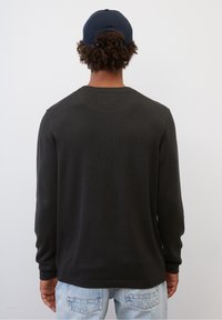 Schwarzes langärmliges Shirt mit rundem Ausschnitt, getragen mit hellblauen Jeans. Das Shirt hat eine glatte Textur und enganliegende Bündchen.