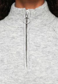 Pulóver de polar gris con un cuello alto, que presenta un cierre de cremallera plateado y un aspecto texturizado. Sin patrones ni acentos distintivos.