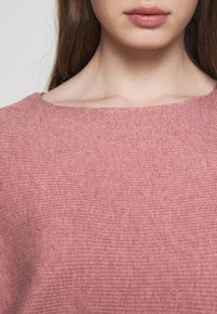 Ljusrosa ribbad stickad topp med vid halsringning och strukturerad tyg, med synliga horisontella linjer och en mjuk, slät yta.