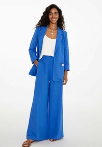 Modrá sako a široké nohavice z ľahkej tkaniny. Sprievodný biely top. Výrazná vrecko na sakovom a béžové sandále.