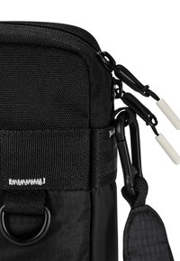 Borsa in tessuto nero con superficie testurizzata, chiusura con zip, due cursori con zip, moschettone laterale e un anello per il fissaggio o l'appensione.