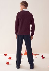 Bordó kötött pulóver bordázott mandzsettákkal, fekete nadrággal párosítva. A modell hátulról látható, egyszerű gallérral és laza szabással.