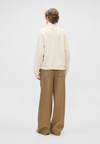 Sudadera beige de gran tamaño con cuello redondo, combinada con pantalones marrones de corte holgado con bolsillos traseros. Tejido de textura suave.