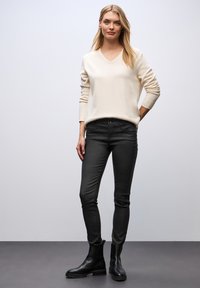 Beige svetr s výstřihem do V spárovaný s černými úzkými kalhotami a černými kotníkovými botami. Hladká pletená textura a štíhlý silueta. Jednoduchý design, bez zdobení.