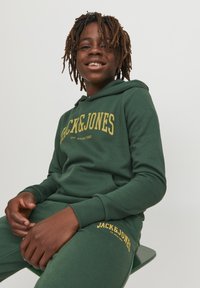 Conjunto de sudadera con capucha y pantalones de chándal verdes, fabricado en algodón, con texto de logo amarillo, puños acanalados y capucha ajustable con cordón.