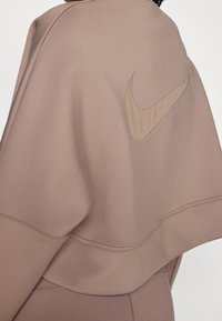 Sweatshirt Nike marron à texture lisse, coupe oversize, avec un logo proéminent dans le dos arborant un design en ton bois plus clair.