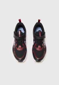 Une paire de chaussures de sport pour enfants noires et rouges avec des semelles blanches, des bandes auto-agrippantes et des logos swoosh de Nike, vues de dessus sur un fond blanc.