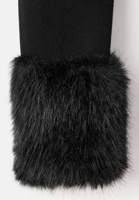 Calentador de piernas de tela negra con un puño de pelo sintético negro y esponjoso. La textura es suave con largas hebras, en contraste con el suave tejido superior.
