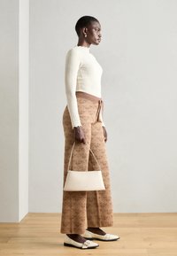 Haut long à manches ribbed crème, pantalon large à motifs beige, chaussures plates blanches avec boucle et un petit sac à main beige.