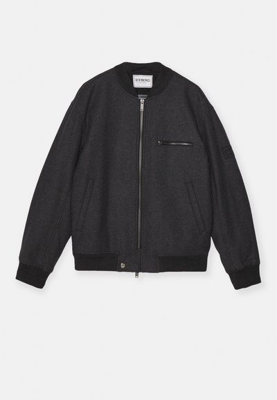 Chaqueta bomber negra hecha de tela texturizada, con cremallera frontal, bolsillos laterales y un pequeño bolsillo en el pecho con cremallera. Puños y dobladillo acanalados.