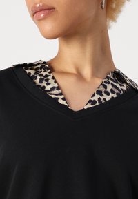 Črn top z V-izrezom in ovratnikom z leopardjim vzorcem. Gladko blago z kontrastnimi teksturami. Kratki rokavi, prilegajoč silhueta.