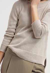 Helle beige Strickjacke mit rundem Halsausschnitt, Rippdetails am Kragen und an den Bündchen sowie einem leicht verlängerten hinteren Saum.