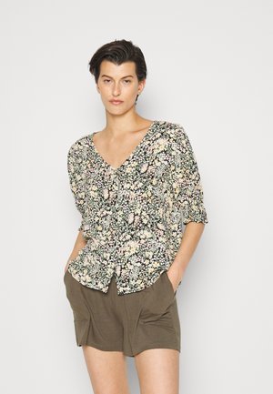 Blusa floral com decote em V, com mangas curtas e bufantes, fundo preto e pequenas flores rosas e amarelas. Combinada com calções em tom de azeitona.