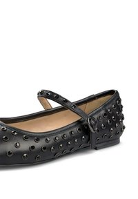 Bailarinas negras de cuero, con una tira sobre el empeine, adornadas con tachuelas redondas negras a lo largo de la parte superior.