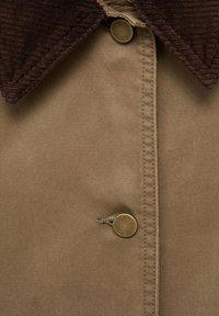 Veste marron avec un col en velours côtelé marron foncé, boutons-pression en métal et couture visible le long de la patte de boutonnage.