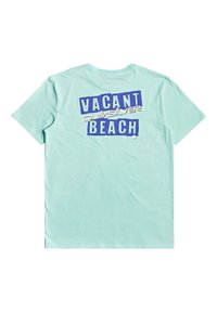 Světle modré tričko s krátkým rukávem, na zádech s tučným fialovým a bílým textem "VACANT BEACH" a logem "Quiksilver".