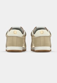 Μπεζ αθλητικά παπούτσια με άνω μέρος από λείο δέρμα και ύφασμα, αντίθετες λευκές λεπτομέρειες, στρογγυλεμένη μύτη και υφασμένο καουτσούκ σόλα. Λεπτομέρεια χρυσού λογότυπου στη φτέρνα.