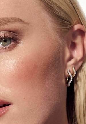 Guld- og sølvøreringe i bølgeform med glitrende detaljer, der har en poleret overflade og indviklet udsmykning.