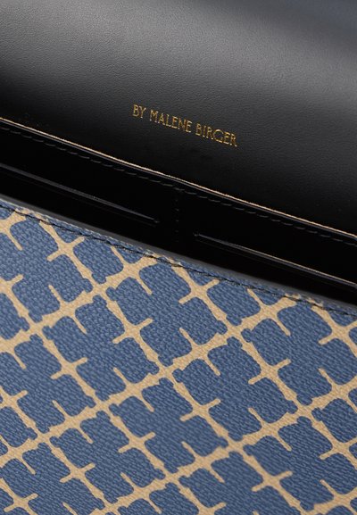 Μπλε και μπεζ υφαντό υλικό με μοτίβο και υφή, με μαύρο δερμάτινο πάνω μέρος και ανάγλυφο χρυσό λογότυπο.