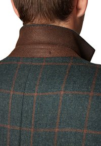 Ciemnozielony płaszcz z mieszanki wełny z brązowym skórzanym kołnierzem oraz czerwono-beżowym wzorem w kratę. Widoczne przeszycia na kołnierzu i faktura materiału.