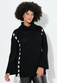 Schwarzer Strickpullover mit hohem Kragen, ausgestattet mit weißen X-Stich-Details entlang der Seite und Glockenärmeln. Weiche Textur, lässige Passform.