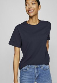 Marineblå kortermet T-skjorte laget av glatt bomullsstoff. Rund hals, avslappet passform med minimale sømdetaljer. Kombinert med blå jeans.