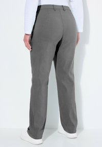 Pantaloni grigi con un design a gamba dritta, realizzati in tessuto morbido, dotati di cintura con passanti e tasche posteriori. Indossati con sneaker bianche.