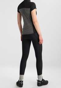 Černé sportovní legíny s přiléhavým střihem, doplněné krátkým tričkem s šedým zadním panelem a strukturovanými detaily.