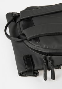 Schwarzer, strukturierter Rucksack mit glatten Lederelementen, einem Traggriff, verstellbaren Trägern und doppeltem Reißverschluss. Kompaktes Design mit minimalem Metallwerk.