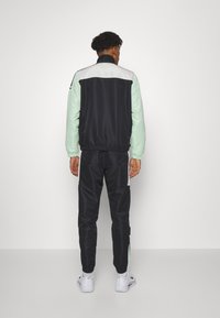 Svart och mintfärgad träningsoverall med dragkedja i kragen, med mintfärgade ärmar och sidopaneler, samt elastiska handleder på byxor och jacka.