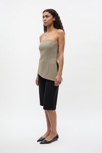 Trägerloses khaki Oberteil mit eckigem Design, kombiniert mit knielangen schwarzen Shorts. Das Model trägt spitze schwarze Schuhe. Glattes, strukturiertes Material.