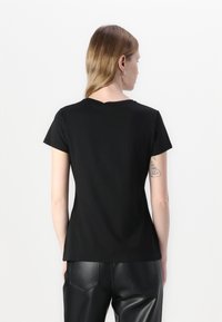 T-shirt nero a maniche corte con scollatura rotonda, design aderente e texture morbida, mostrato da dietro con tatuaggi visibili sul braccio.