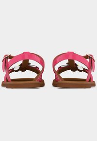 Παιδικά ροζ σανδάλια με καφέ σόλες, διακοσμημένα με λευκά και κίτρινα λουλούδια, απεικονιζόμενα από πίσω σε λευκό φόντο.