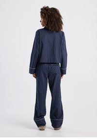 Navy striped loungewear set with a cropped top and wide-leg pants. Features white piping on sleeves and cuffs. Soft fabric with a relaxed fit.