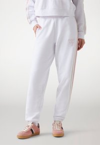 Witte sweatpants met zijstrepen in roze en crèmekleur, een elastische tailleband en zakken. Gecombineerd met roze sneakers met donkere accenten.