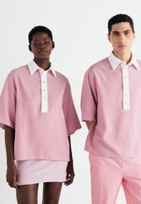 Rózsaszín, textúrázott, túlméretezett pólóingek fehér gallérral és gombos légzéssel, rózsaszín szoknyával és illő nadrággal párosítva.