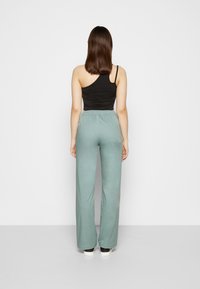 Top preto de um ombro só combinado com calças largas de cor verde claro, com um cós elástico e bolsos laterais. Textura suave.