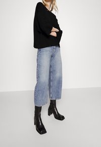 Czarny, oversize'owy top z długim rękawem, zestawiony z niebieskimi, średniowysokimi, krótko przyciętymi dżinsami oraz czarnymi, na obcasie botkami za kostkę. Gładkie tkaniny i dopasowany, strukturalny krój.