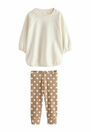 Cremefarvet langærmet skjorte kombineret med beige ribstrikkede leggings med store hvide polkaprikker og knapdetaljer ved manchetterne.