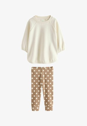 Cremefarvet langærmet skjorte kombineret med beige ribstrikkede leggings med store hvide polkaprikker og knapdetaljer ved manchetterne.