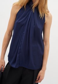 Marinblus utan ärmar med plisserad front, hög krage och slät tyg. Har en avslappnad passform och subtil lyster. Skräddarsydd design.