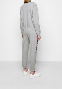 Grijze sweatshirt en bijpassende joggers gemaakt van zachte stof. De sweatpants hebben de tekst "NO PRIM" aan de zijkant. Gecombineerd met witte sneakers.